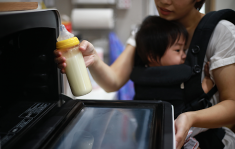 Mother heating up infant milk in microwave.