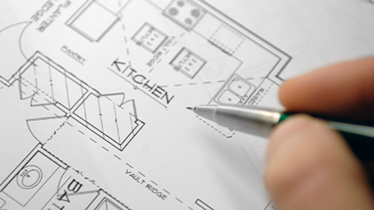 Selective focus image of architectural drawings and hand holding mechanical pencil.