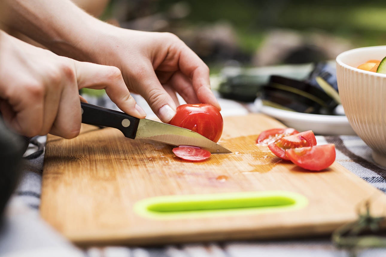 Person cutting tomato on wooden board.