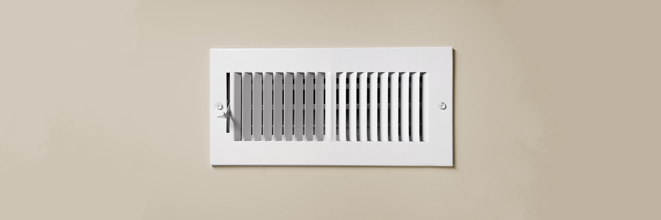 A cooling vent register on the wall of a home, with open lever.