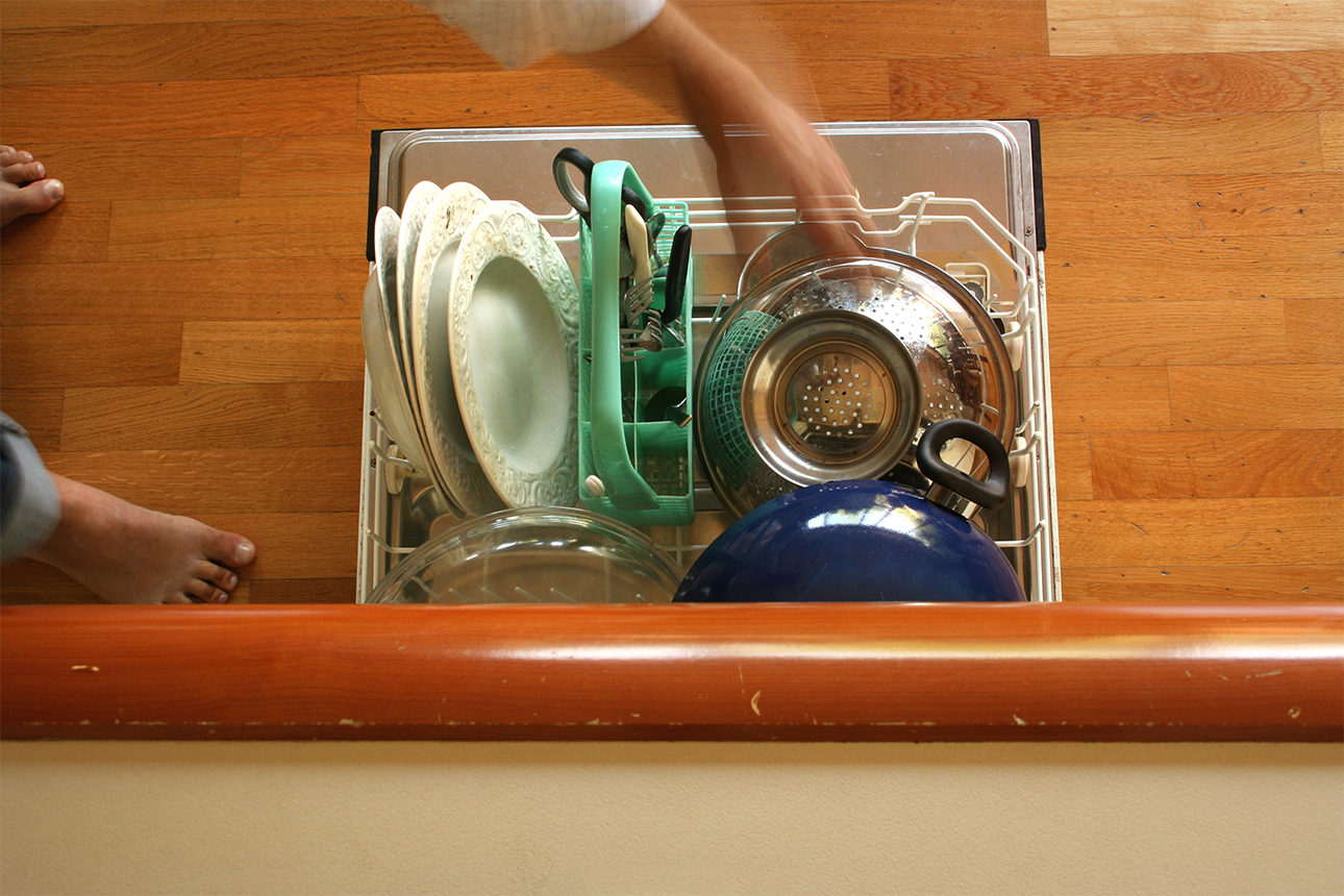 A men's hand is putting dirty items in a dishwasher.