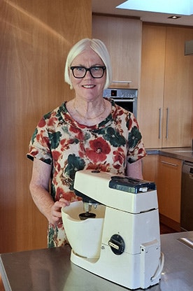 Lady standing behind a cake mixer on a table.