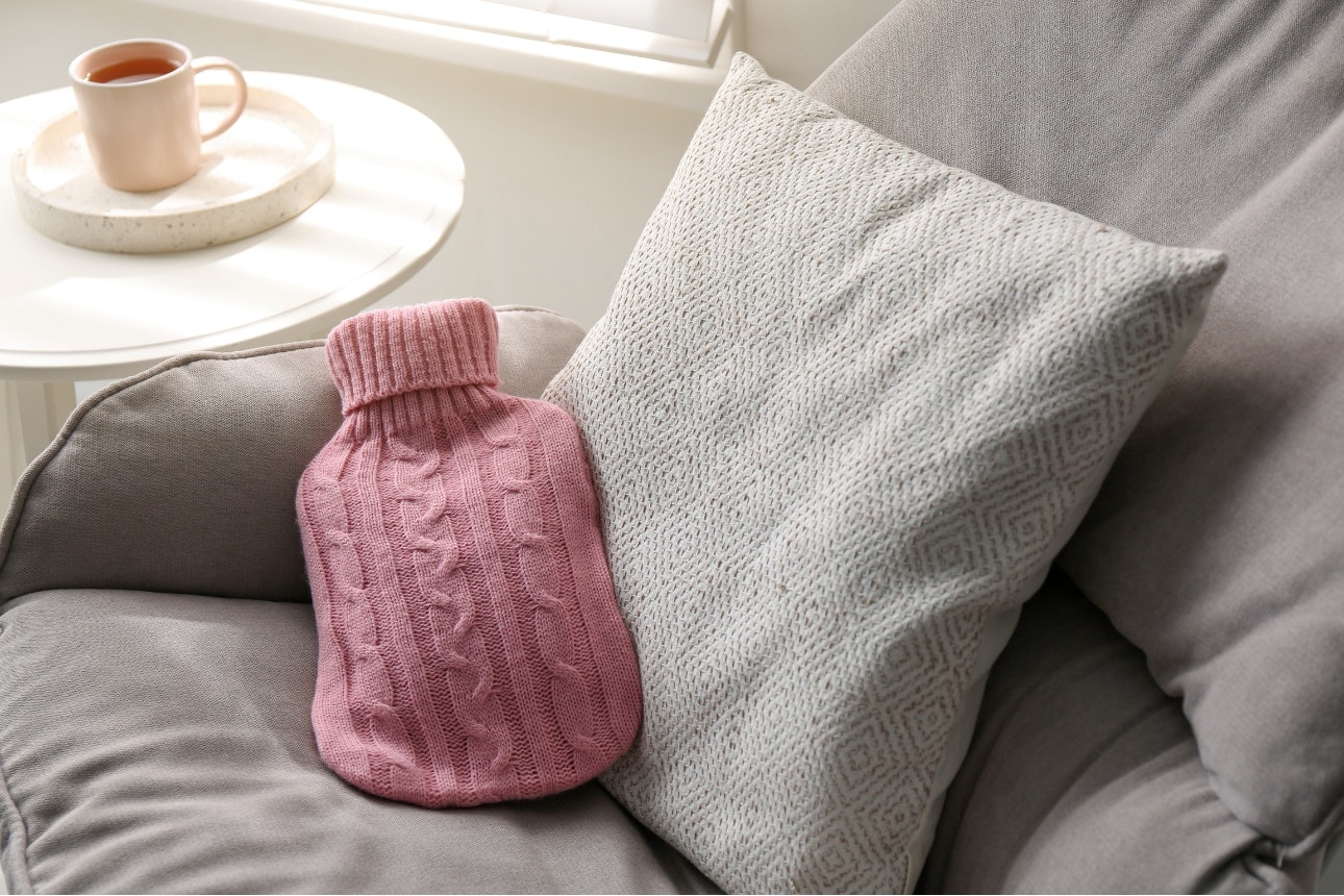 Pink hot water bottle on grey couch.