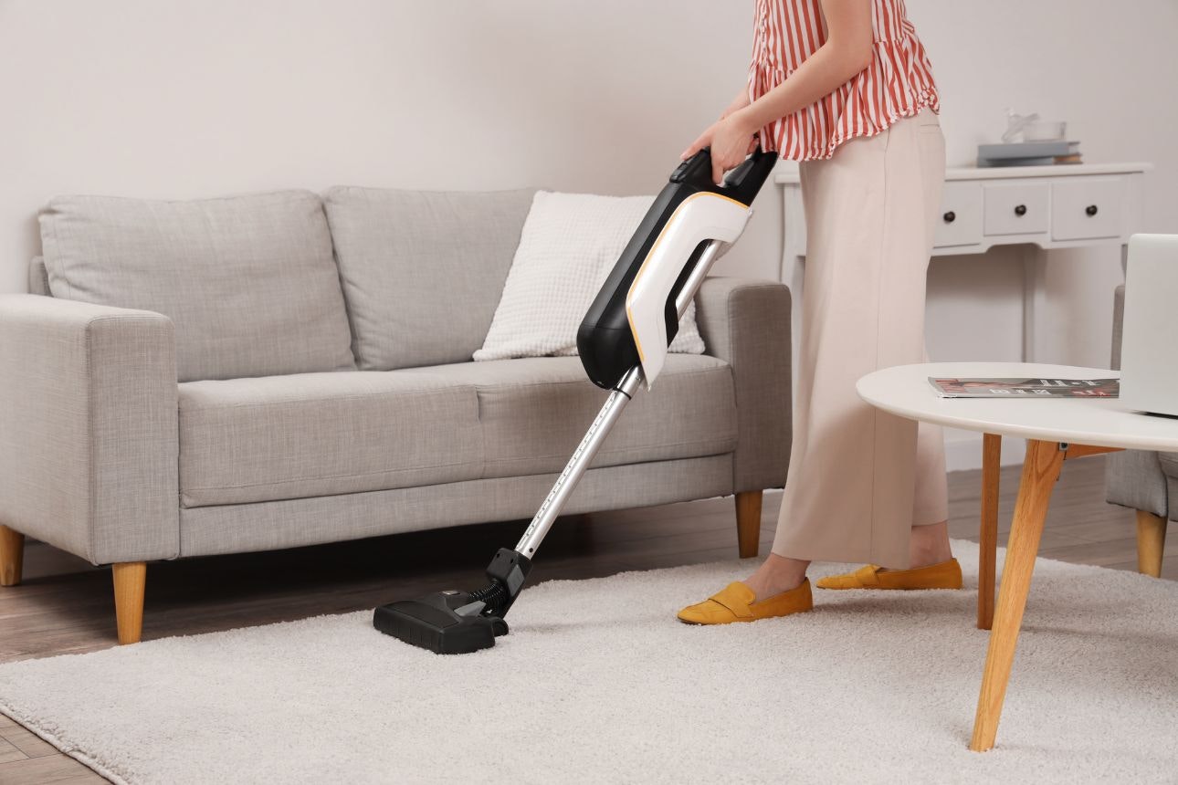 Woman using stick vacuum on carpet.