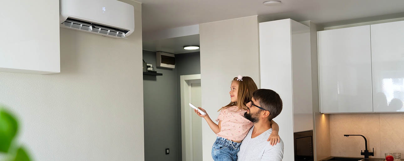 Father holding daughter who is adjusting heat pump with remote.