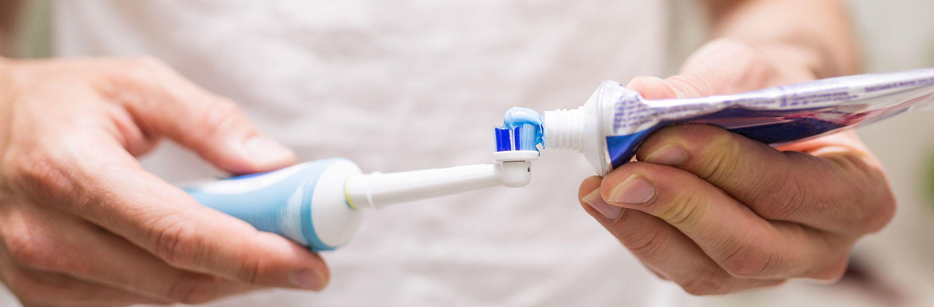 Man putting toothpaste onto electric toothbrush