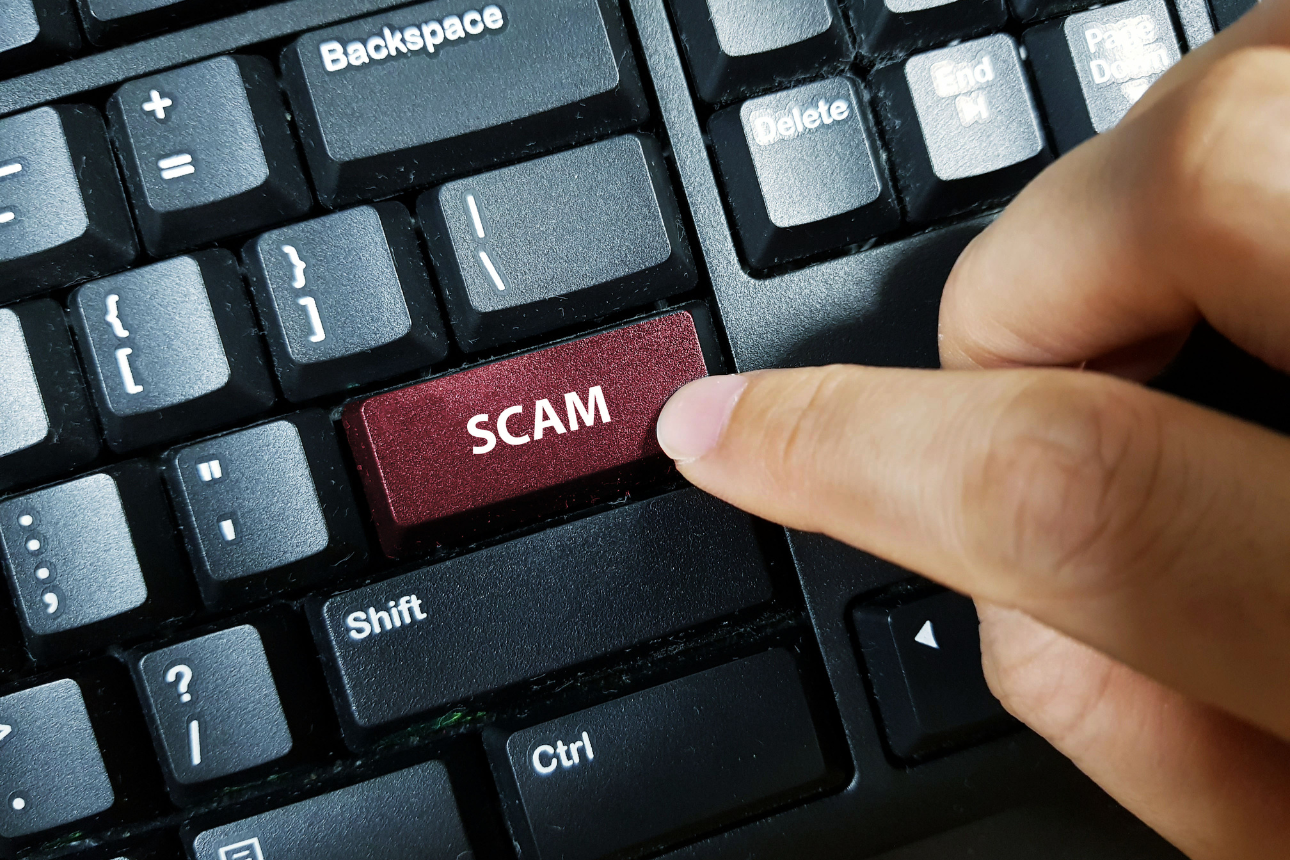 Person pressing 'scam' button on computer keyboard.