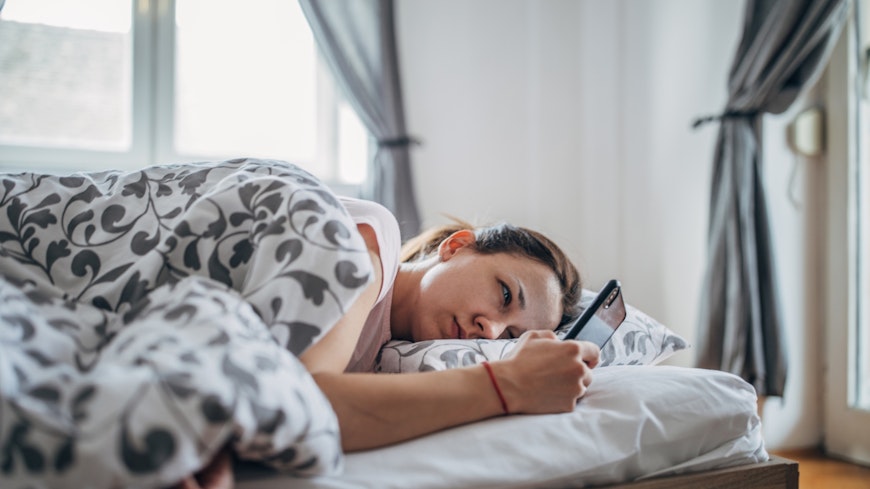 Woman laying in bed using smartphone.