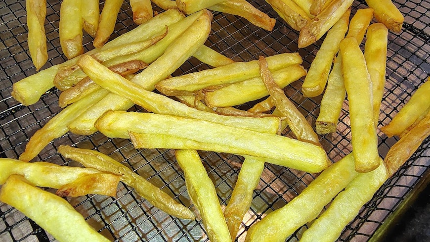 Cooked chips in an air fryer basket.
